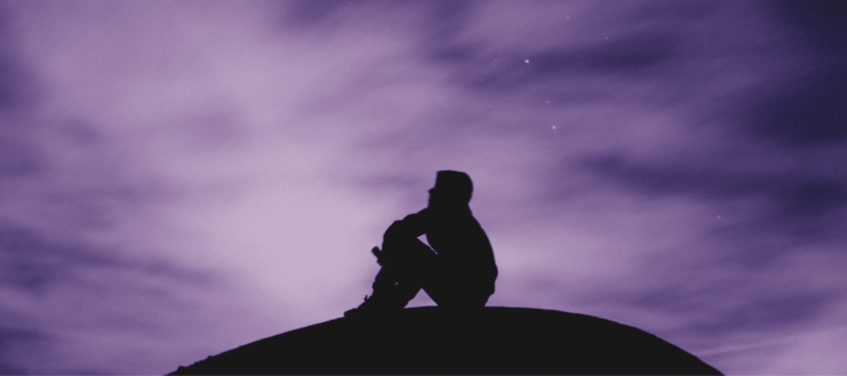 A man sits atop a hill at twilight, thinking