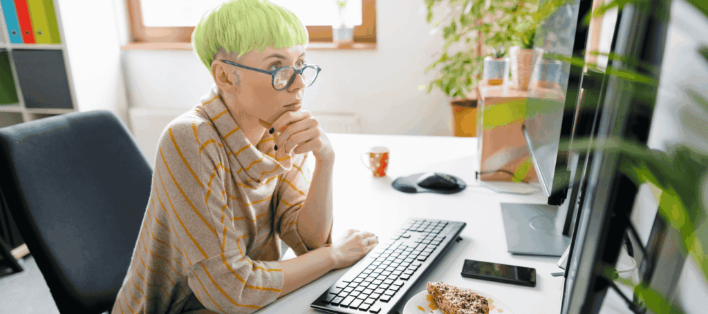 A girl sits at her desk in a sunny room at home concentrating on the big screen in front of her.