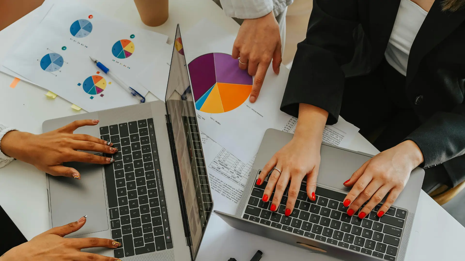 Person typing on a laptop with financial reports, spreadsheets, and a pie chart on the desk—suggesting business planning or financial analysis in a work or study setting.