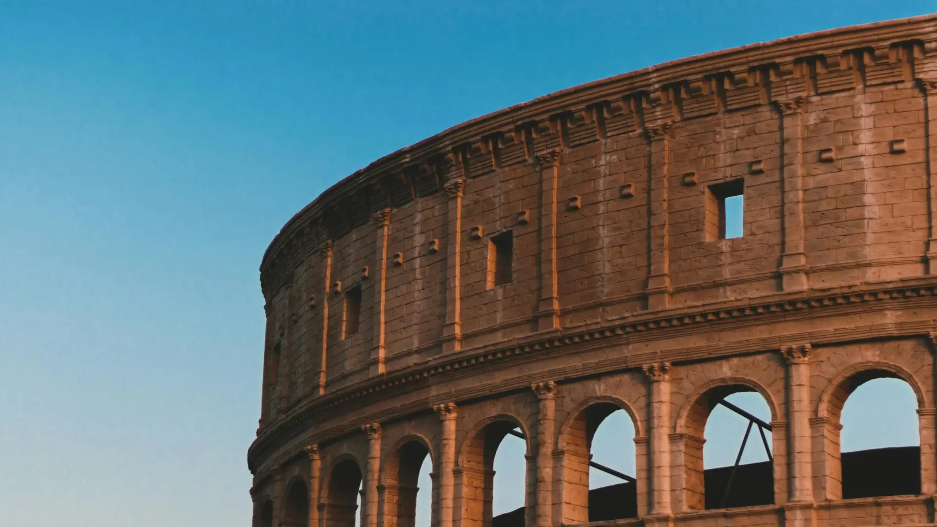 A close-up view of the ancient Roman Colosseum under a clear blue sky, showcasing its iconic arches and stone architecture.