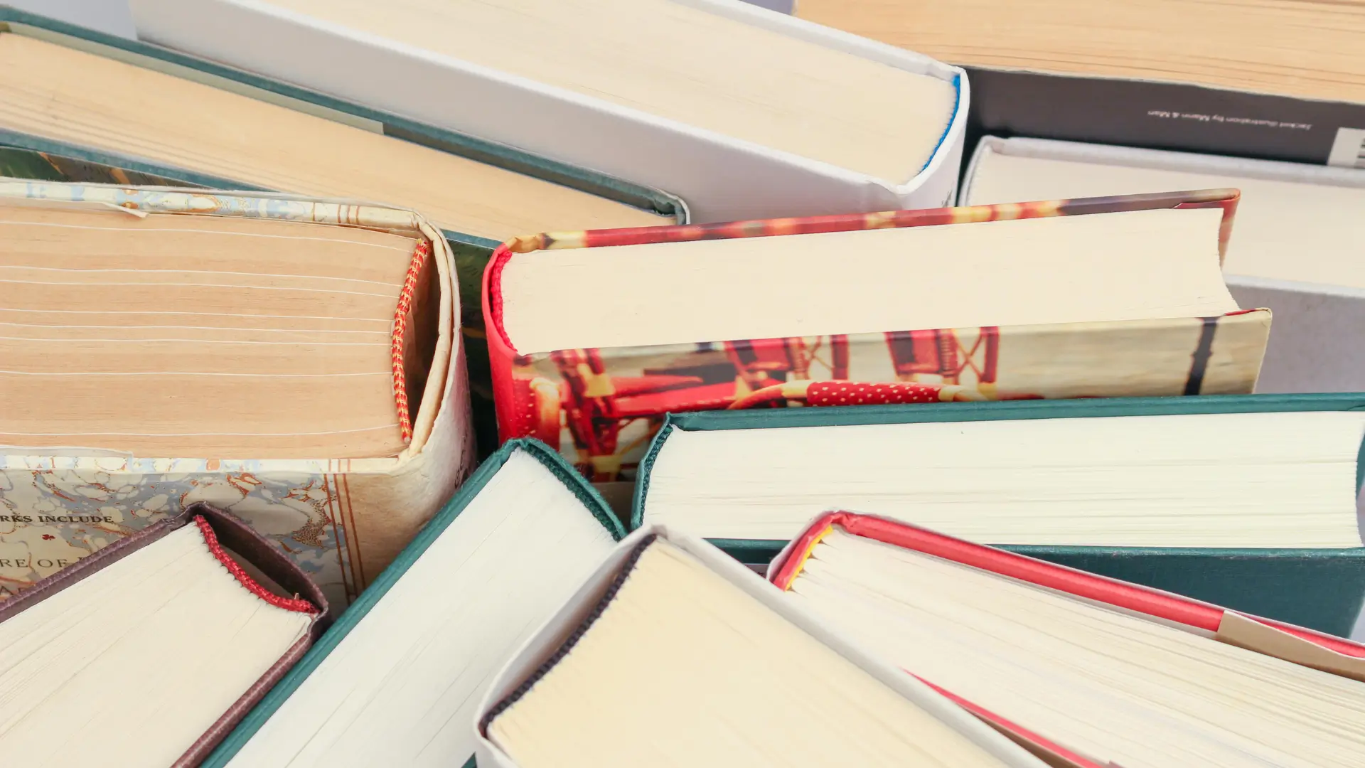 A close-up view of the tops of several stacked hardcover books with colourful bindings, representing a collection of classic and contemporary literature.