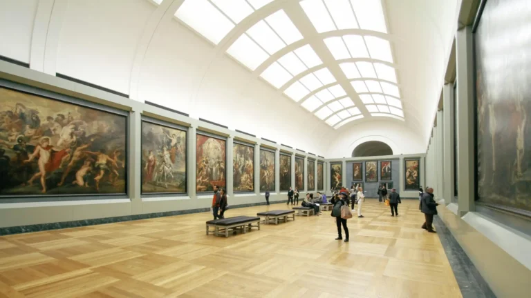 Visitors walking through an art gallery with large classical and Renaissance paintings displayed on both sides, representing the study of art history and visual culture.