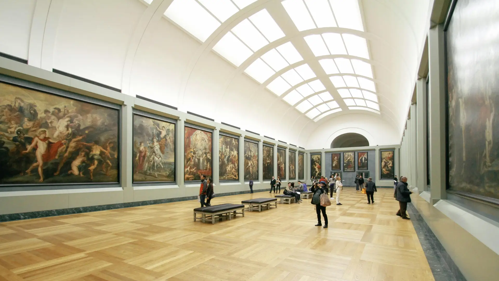 Visitors walking through an art gallery with large classical and Renaissance paintings displayed on both sides, representing the study of art history and visual culture.