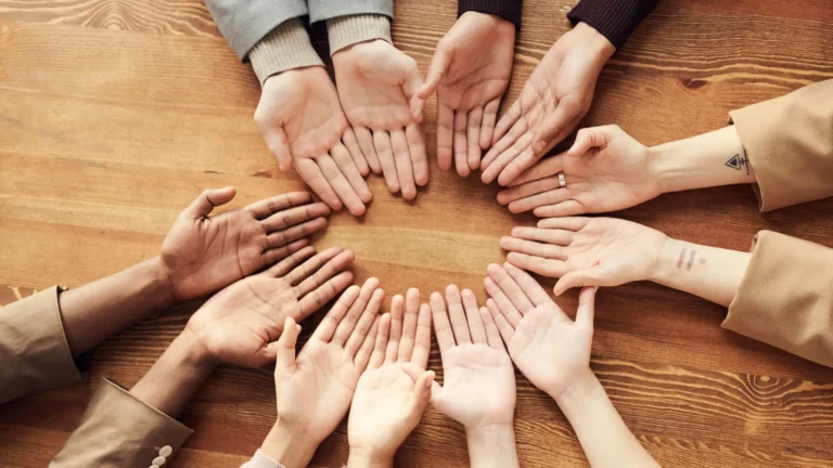 A group of diverse hands arranged in a circle on a wooden table, symbolising unity, inclusion, and social connection—key themes in sociology.