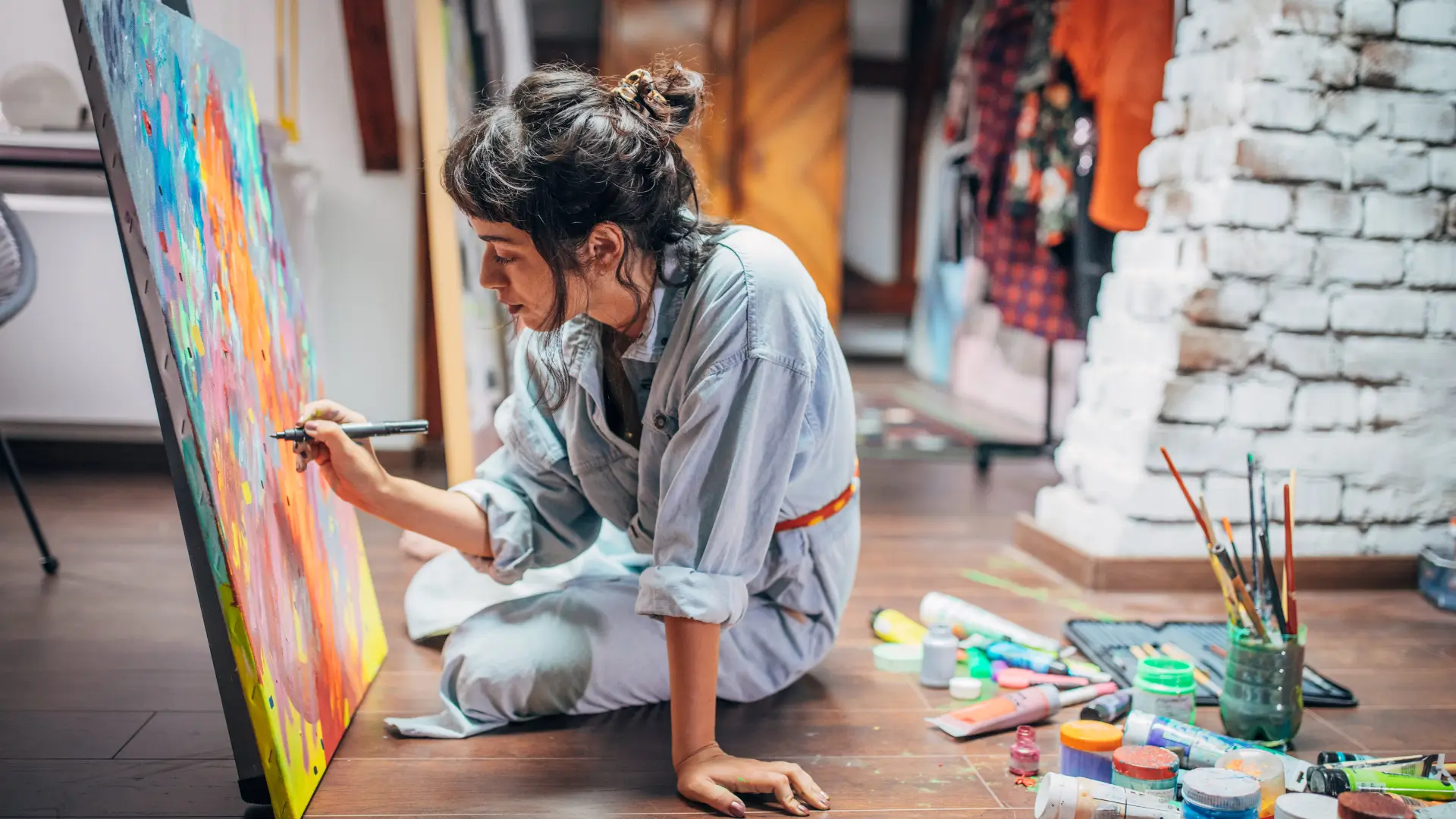 Woman sat on floor painting on a canvas with oil paints.