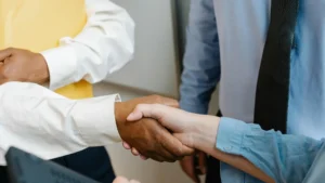 Close-up of diverse professionals shaking hands in a workplace setting, representing leadership, teamwork, and management development.