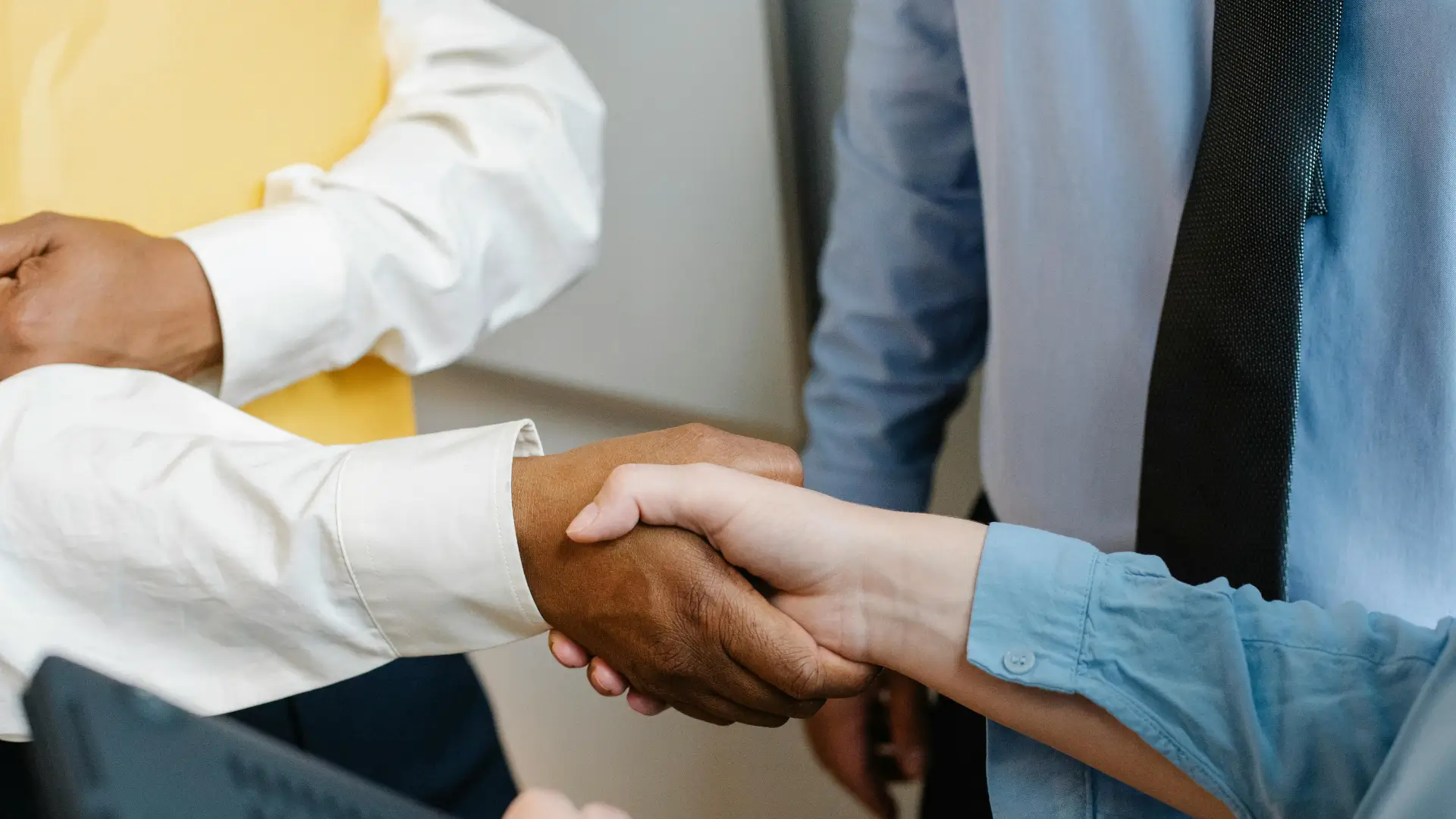 Close-up of diverse professionals shaking hands in a workplace setting, representing leadership, teamwork, and management development.