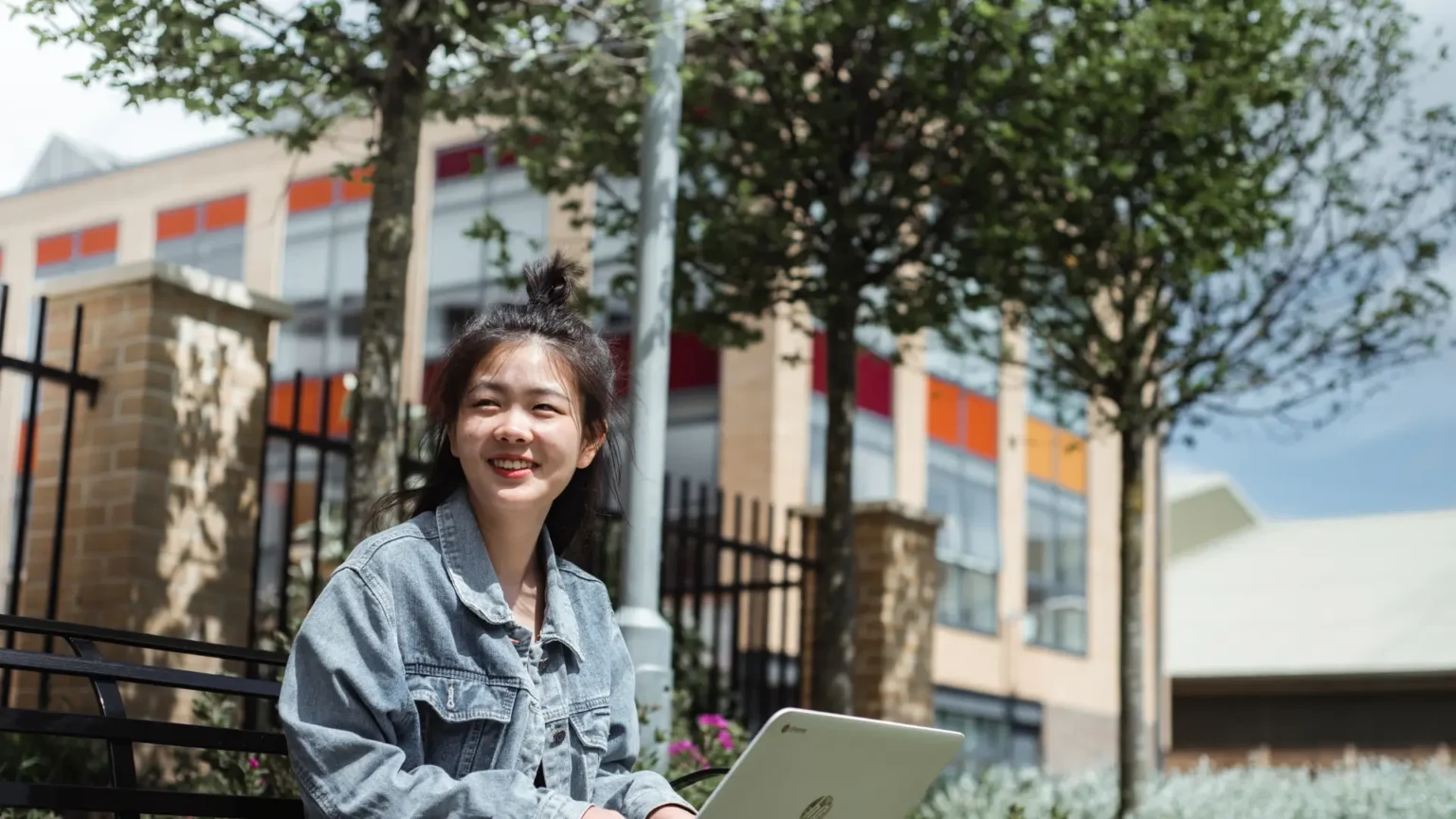 Young student smiling outdoors while working on a laptop, symbolising the flexibility and independence of NEC’s online Fast Track A level programme.