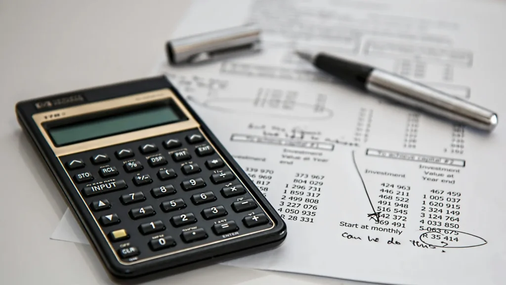 Close-up of a calculator and financial documents used in bookkeeping, alongside a pen and handwritten notes.