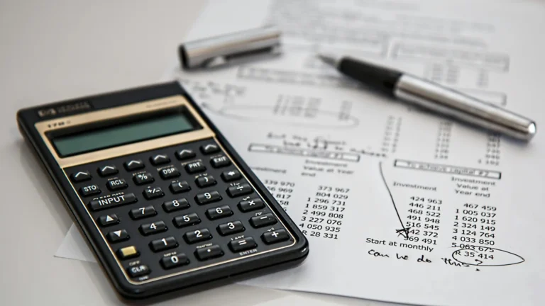Close-up of a calculator and financial documents used in bookkeeping, alongside a pen and handwritten notes.