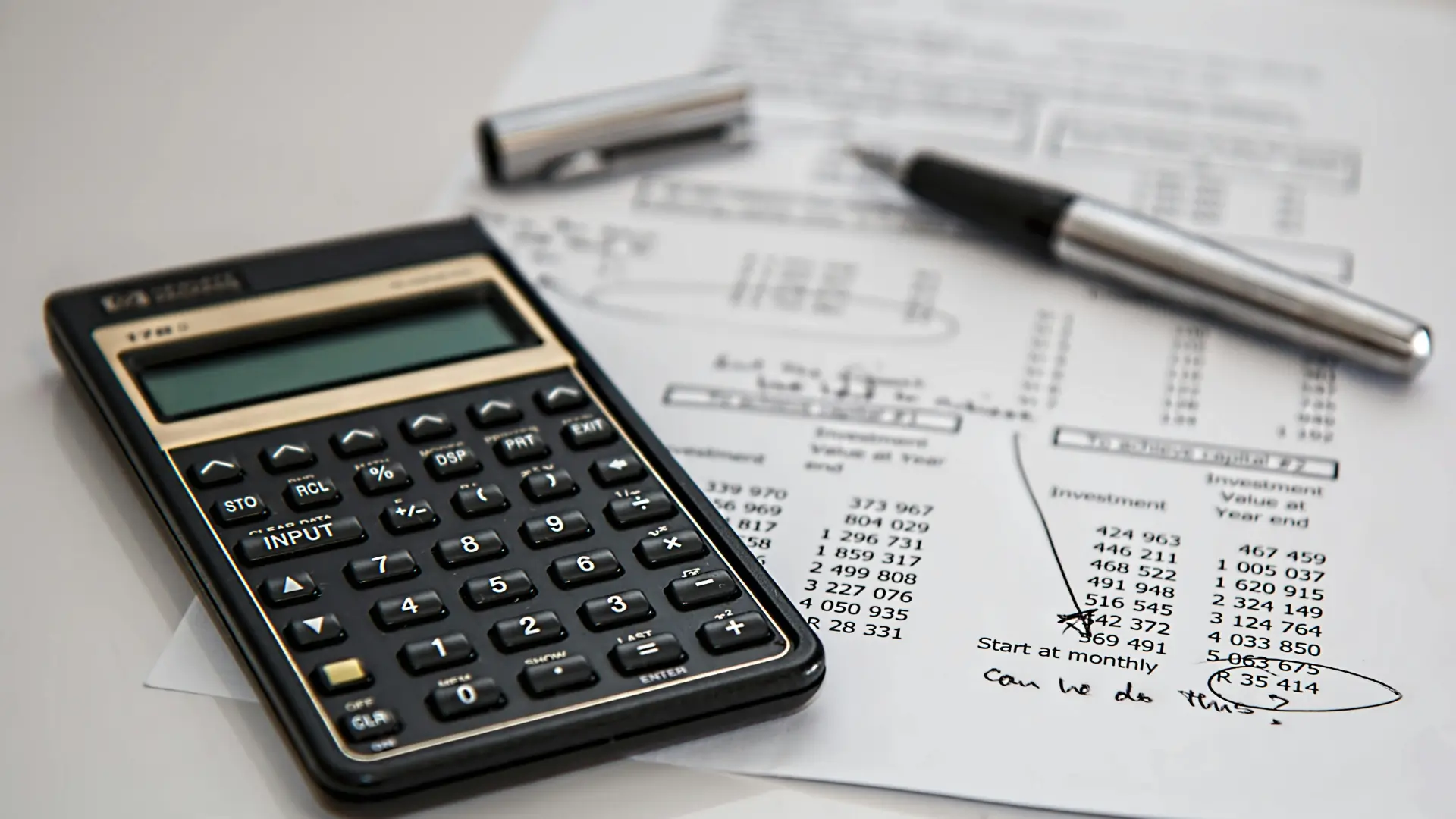 Close-up of a calculator and financial documents used in bookkeeping, alongside a pen and handwritten notes.