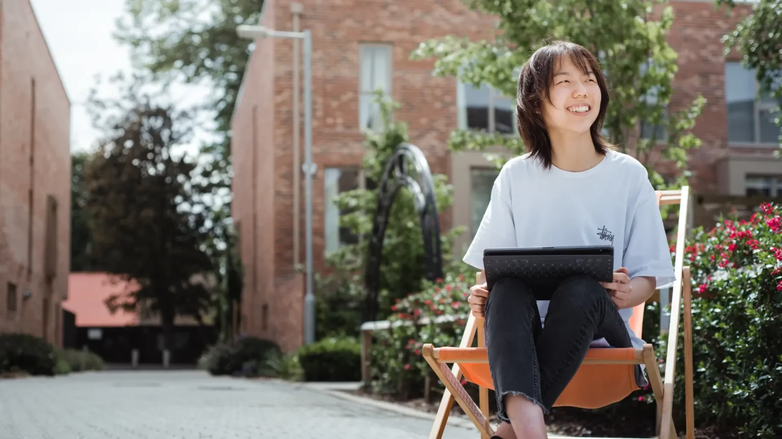 A smiling student studying outside with a tablet, representing flexible online learning for international A level students