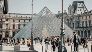 A busy day outside the Louvre Museum in Paris, with the iconic glass pyramid in view and people walking through the square—highlighting the cultural appeal of learning a new language for travel and connection.
