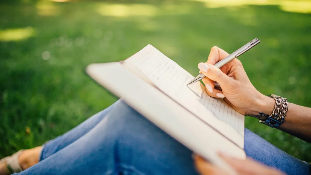Woman sat on the grass writing in a notepad.