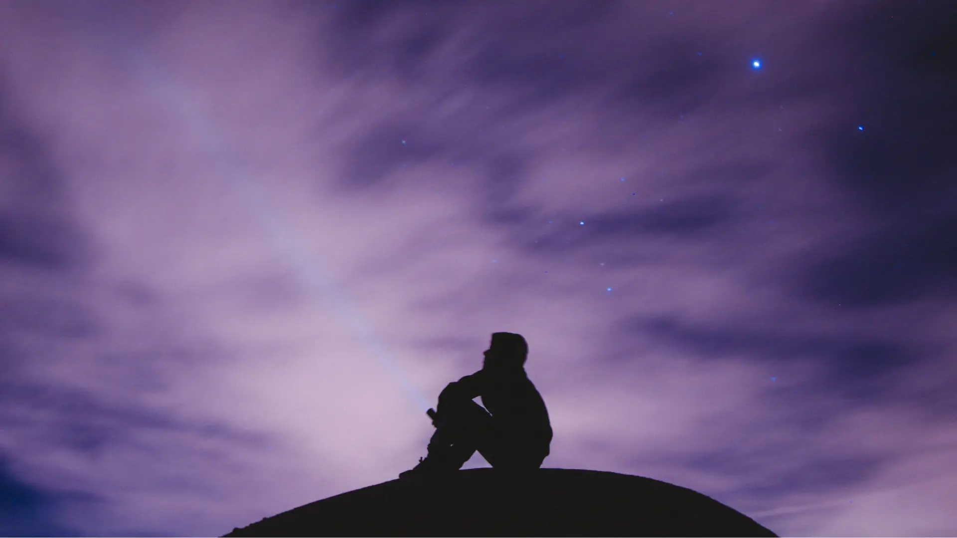 A man sits atop a hill at twilight, thinking