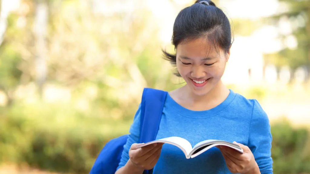 Smiling lady waiting outside smiles as she looks through her study notes.