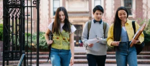 Three smiling teenage students walking together outside their university building