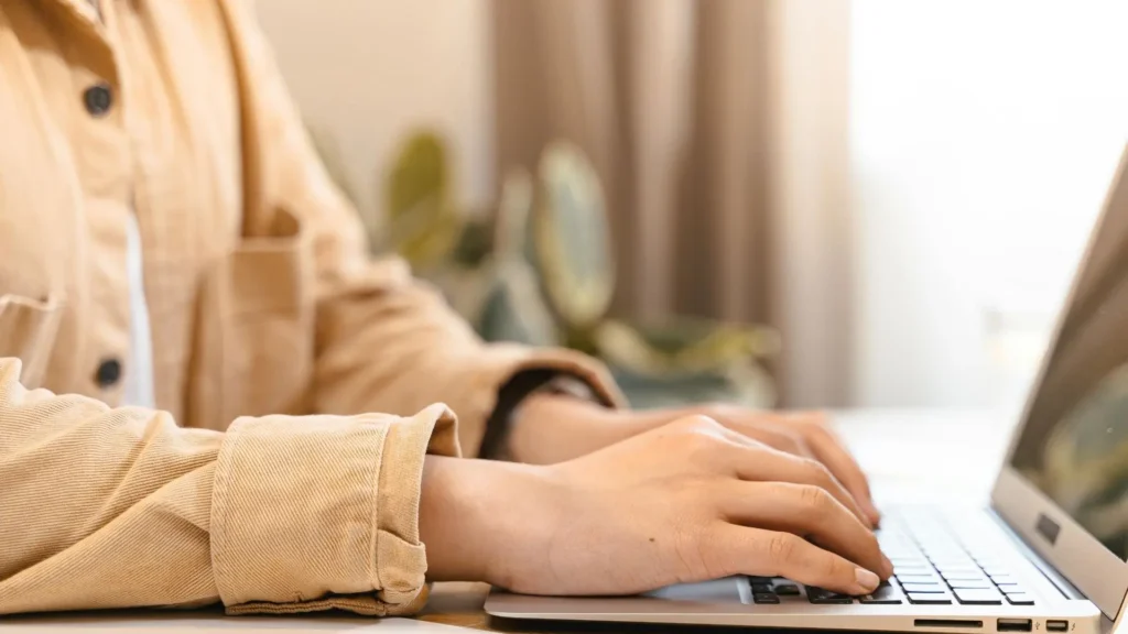 Close-up of a student typing on a laptop while studying online from home.