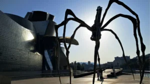 Louise Bourgeois’s giant spider sculpture Maman (1999) outside the Guggenheim Museum Bilbao, silhouetted against the sun with the museum’s curved metallic facade in the background.