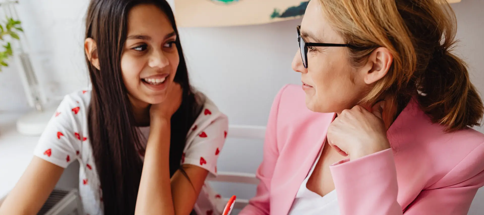 Teenage girl and her mother sitting at a desk and smiling