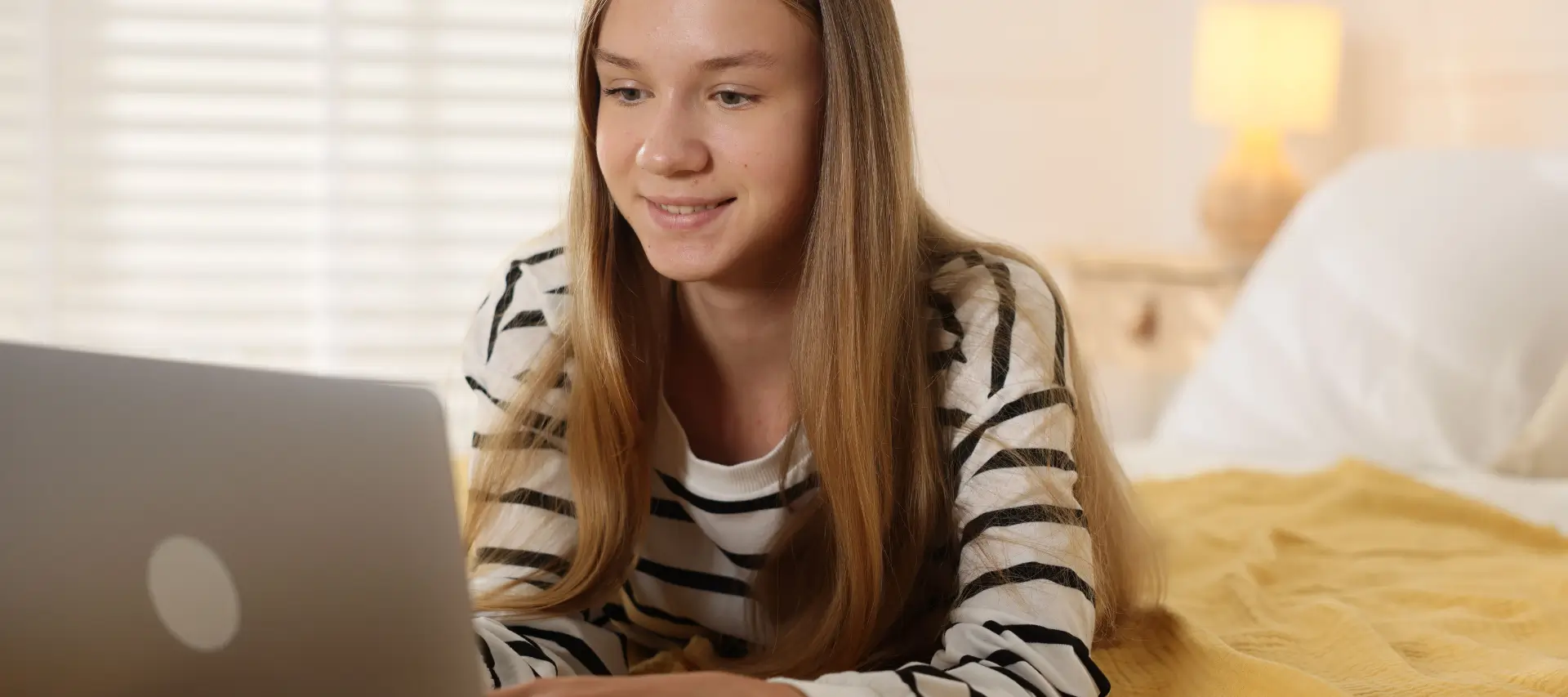 Smiling teenage girl laying on her bed studying at her laptop