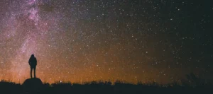 Silhouette of someone standing alone looking at the stars in the night sky.