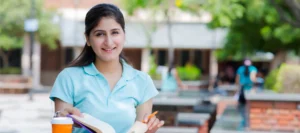 Smiling student in a pale blue t-shirt sits studying in an outside cafe