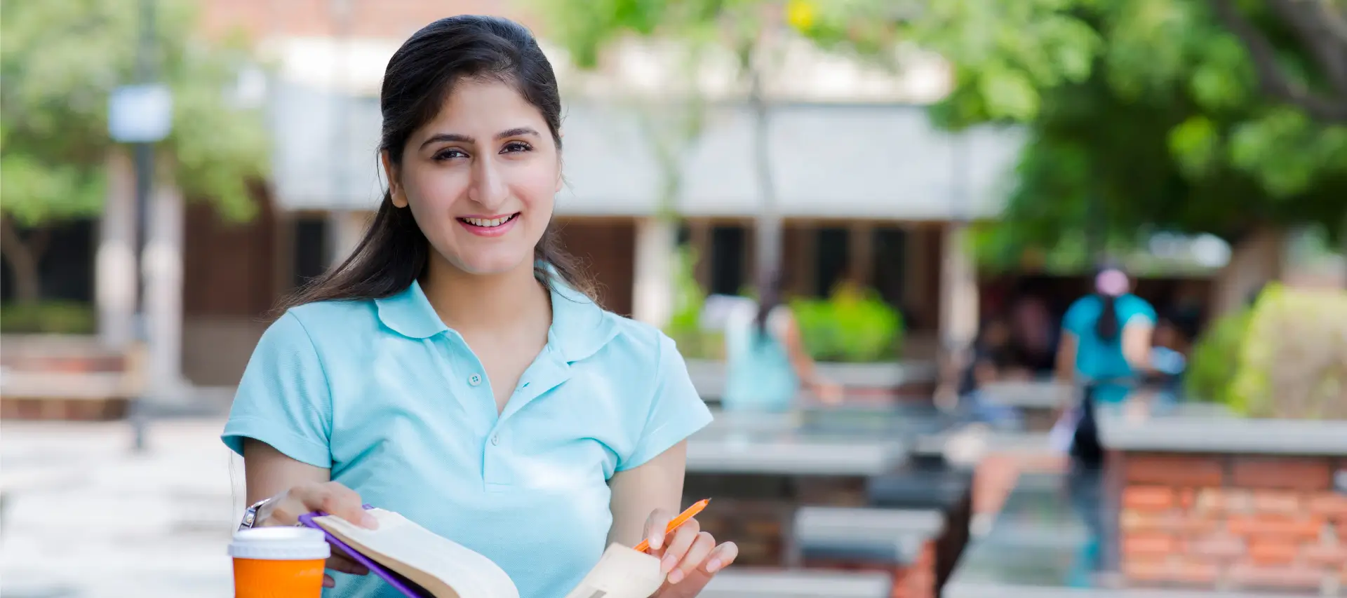 Smiling student in a pale blue t-shirt sits studying in an outside cafe