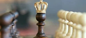 Chess piece wearing a gold crown stands between two rows of other chess pieces