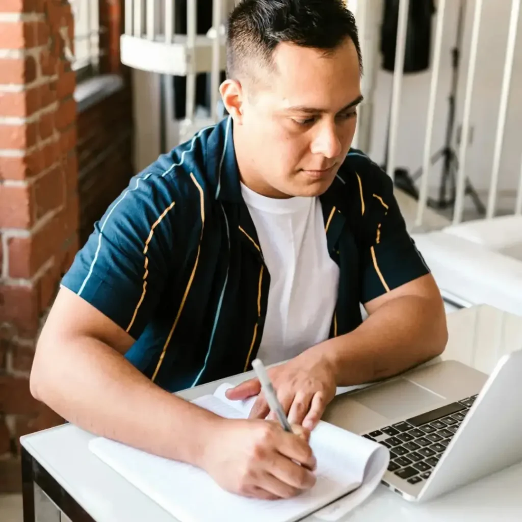 A man sits at his desk studying, with a laptop an a notebook