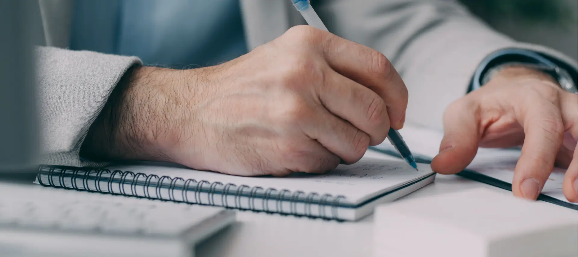 man writing in notepad as he studies online A level English literature