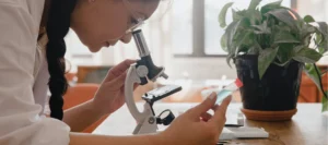 female studying biology at home looking through microscope